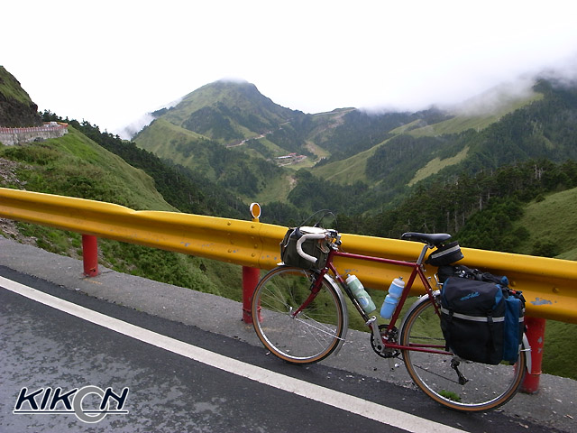 山道にある黄色いガードレールと赤い支柱、そこに自転車を立て掛けて停めている