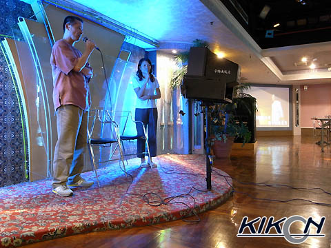 ステージのようになっている場所で、青い照明に照らされながら２人の男女がカラオケで歌っている