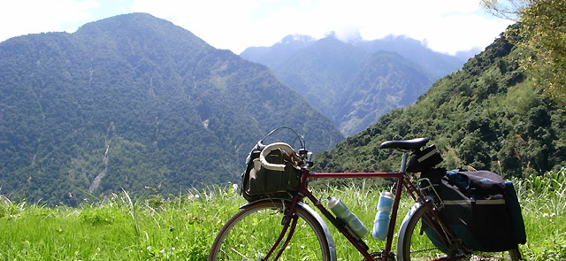 玉山国家公園からの眺望。草むらに自転車が停まっている、彼方に緑の山々の連なりが見える