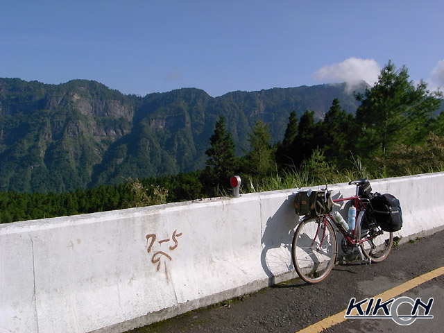 大きなコンクリート製のフェンスのある、阿里山周辺の道路脇に自転車を停め山々を望む