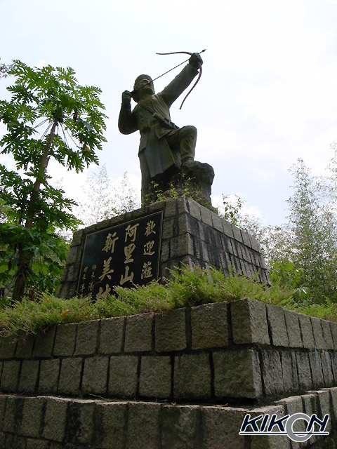新美村の入り口に建つ先住民の像、石垣上の台座のうえに弓を構える男の像がある。台座に「阿里山新美村」の文字。