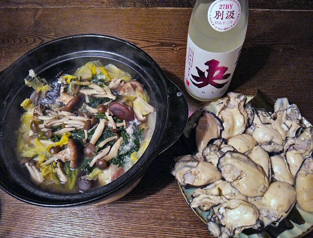 皿の上に酒蒸しの牡蠣の身がびっしり並んでいる。鍋にキノコ（シメジ？）白菜、春菊（？）と汁。日本酒瓶「央」桃ラベル　別汲み